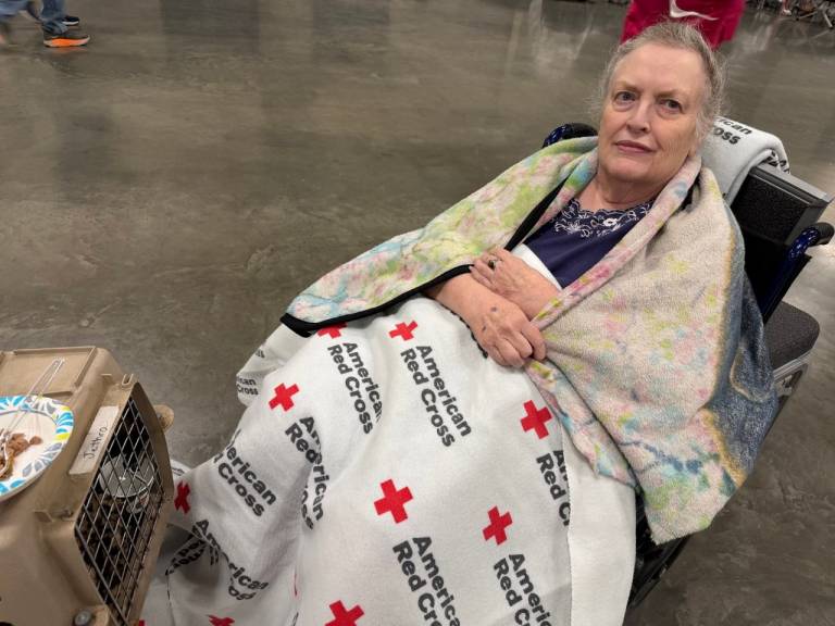 Woman wrapped in Red Cross blanket sits in a shelter.