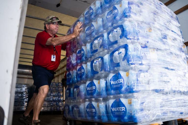 Man in Red Cross shirt moves pallet of cases of water.