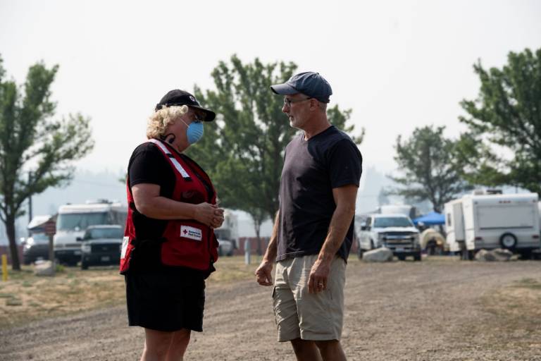 Woman in Red Cross vest speaks with man in shorts.