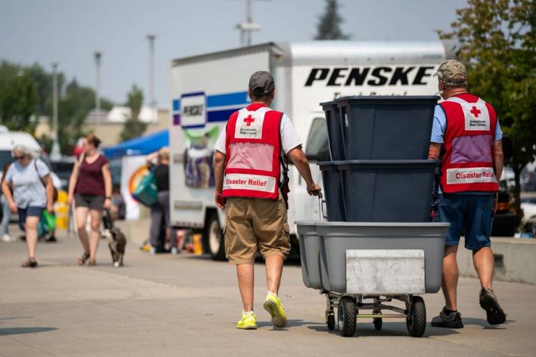 Men in Red Cross vests push dolly with large totes.