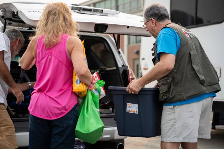 Man in Red Cross vest loads wildfire kit into a couple’s car.