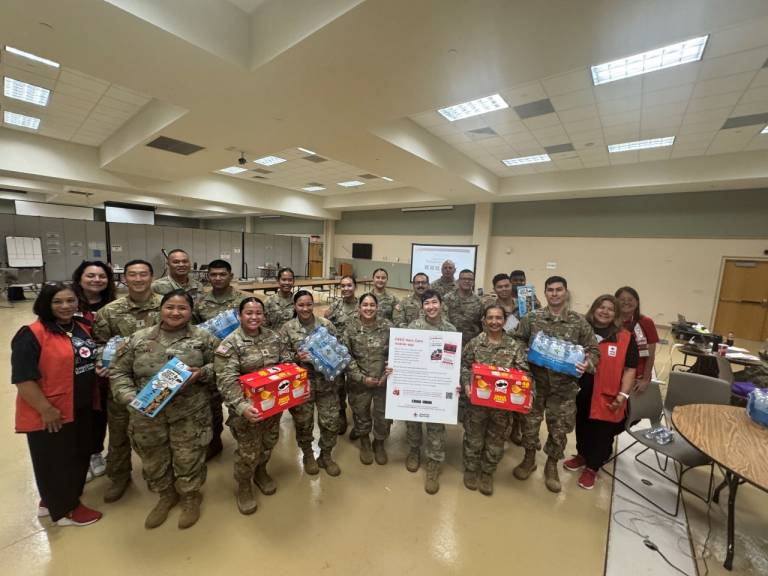 Women in Red Cross vests stand with people in military uniforms.