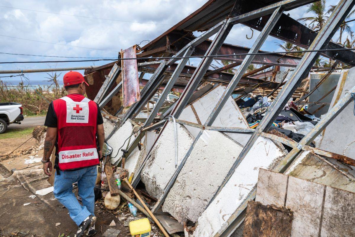Man in Red Cross vest checks damaged homes.