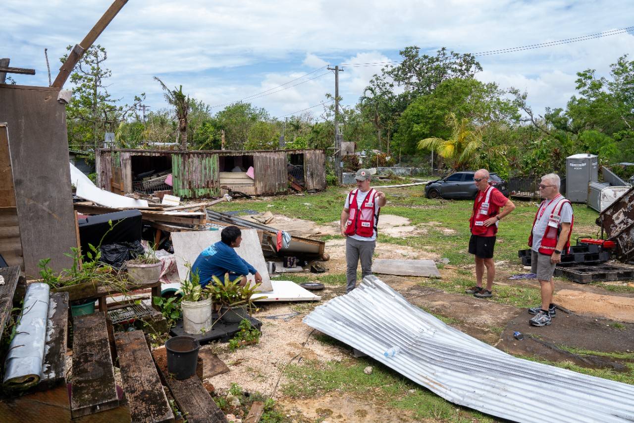 Man sits on steps talking with men in Red Cross attire
