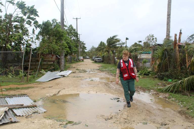Woman in Red Cross vest walks along street filled with debris