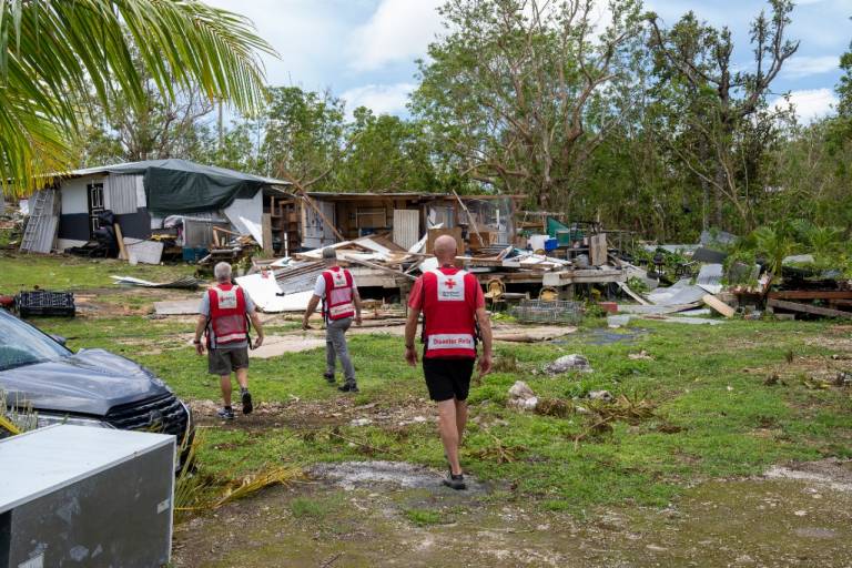 Men in Red Cross shirts walk through storm debris