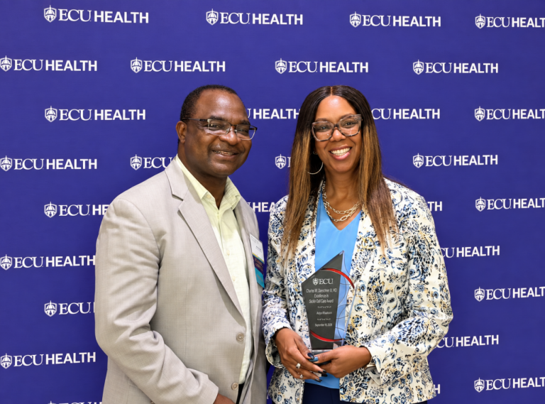 Asiya Khaatoon and Dr. Beng Fuh smile in front of an ECU Health backdrop as she holds her glass award.
