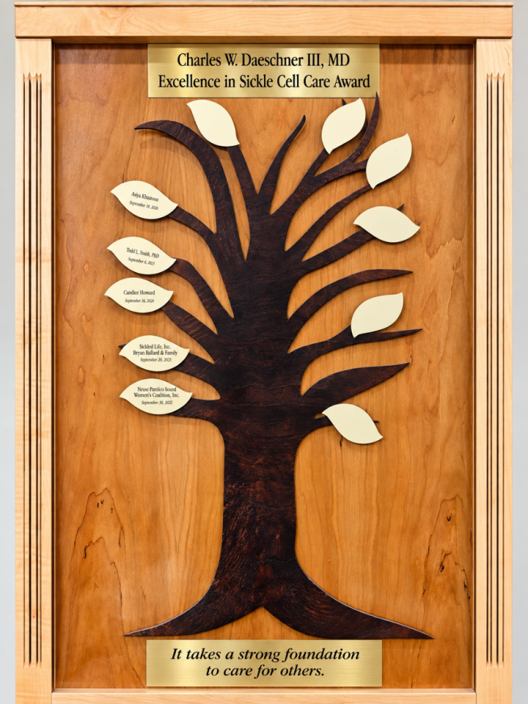 A framed wooden plaque of a carved tree with gold leaves, each bearing an honoree’s name, beneath a title plate reading Charles W. Daeschner III, MD Excellence in Sickle Cell Care Award.
