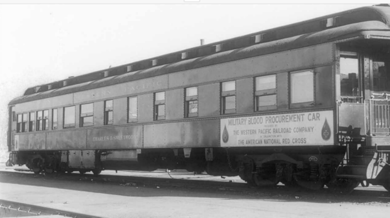 Fotografía en blanco y negro de un antiguo vagón de tren con un rótulo de la Cruz Roja y grandes gotas de sangre