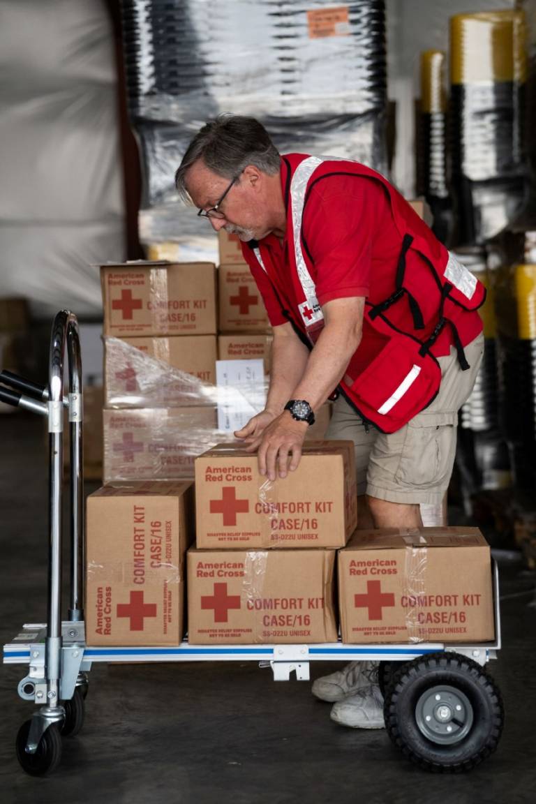 Man in Red Cross vest packs gloves into a tote.