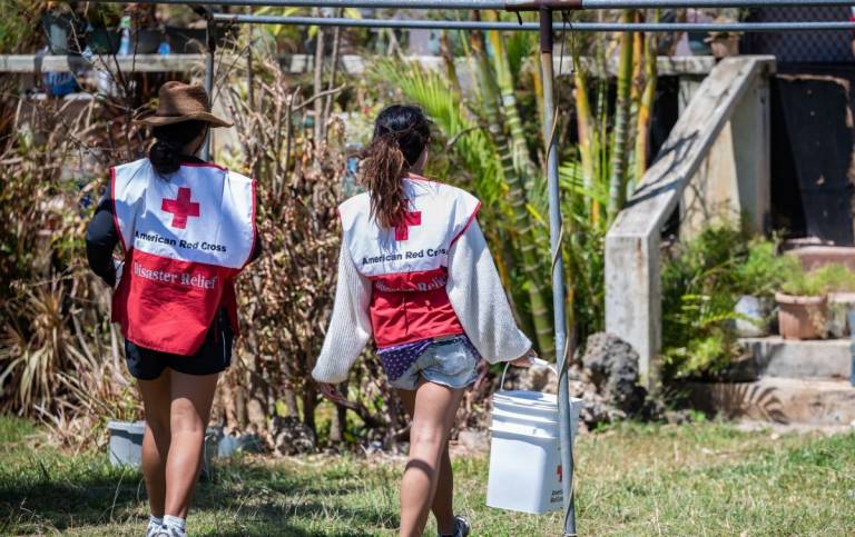 Two women in Red Cross vests deliver relief supplies.