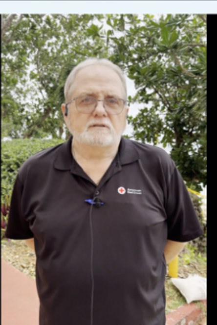  Man in Red Cross shirt speaks to a camera.