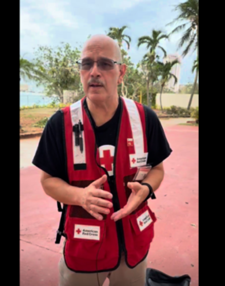 Man in Red Cross shirt speaks to a camera.