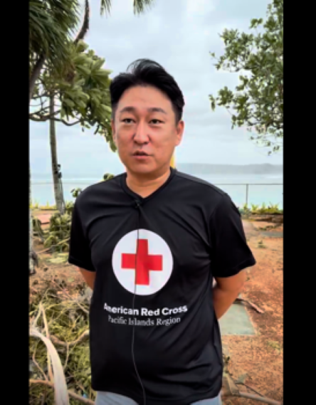 Man in Red Cross shirt speaks to a camera