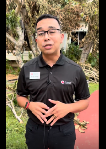 Man in Red Cross shirt speaks to a camera.