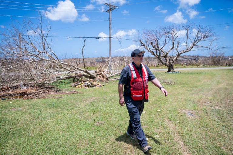 Man in Red Cross vest walks down a street