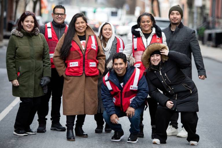 Group of people in winter coats stand on a city sidewalk