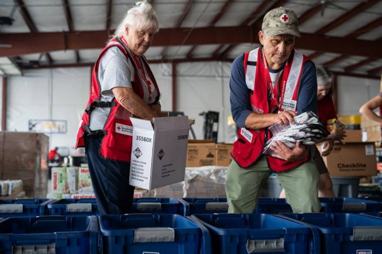 A man and woman in Red Cross vests work at packing wildfire kits to hand out to people in the Spokane area after the wildfires there.