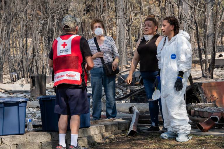 Man in Red Cross vest talks with three women, one wearing a white hazmat suit.