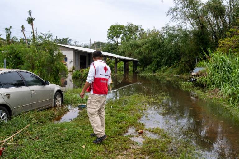 Man in Red Cross vest looks at storm damage.