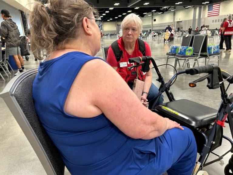 Woman in Red Cross vest sits in shelter with another woman