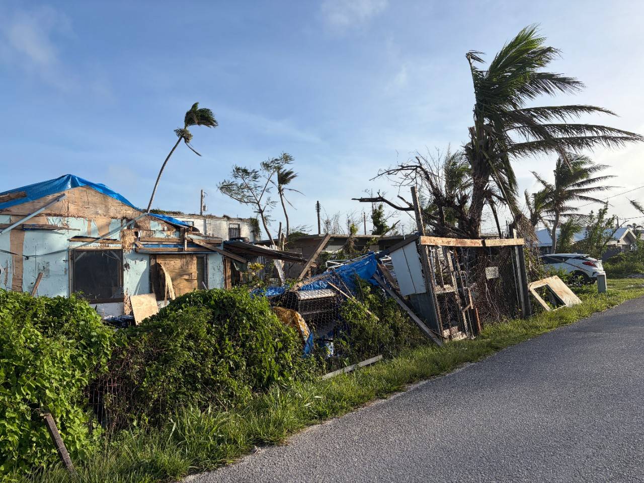 A destroyed home with pieces of blue roof tarp also visible.