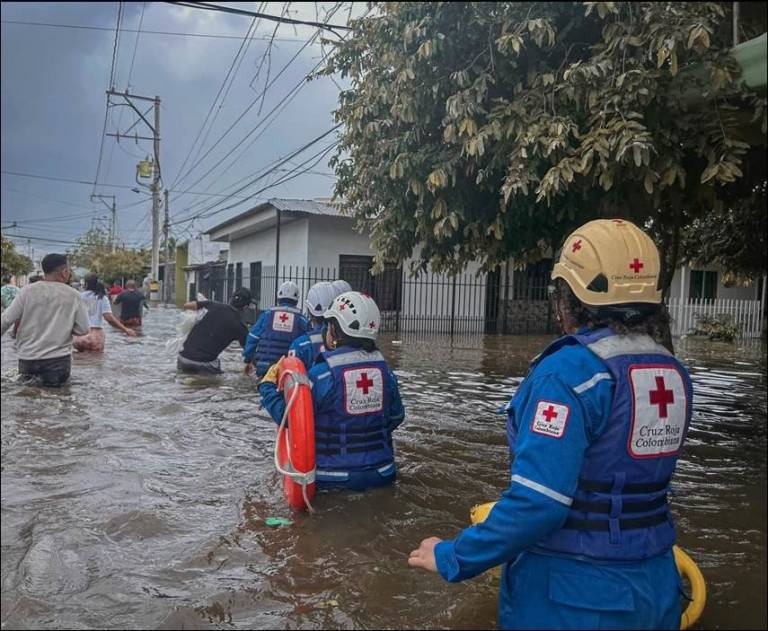 group of people in Red Cross clothing wade through waist deep water