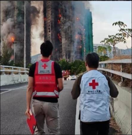 Personas con chalecos de la Cruz Roja se acercan a una torre de apartamentos en llamas.