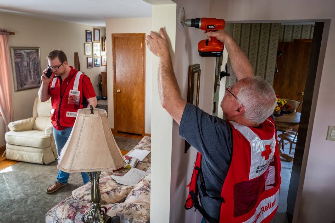 April 28, 2018. Endicott, New York.Smoke Alarm Installations, Sound the Alarm Campaign.Pictured: American Red Cross volunteers Dave Peace and Max Little.American Red Cross Southern Tier volunteer Dave Peace installs a free smoke alarm in a home in Endicott, New York while his teammate, Max Little, takes a call. Dave and Max are volunteering as part of a fire safety promotion called "Sound the Alarm." During this national effort to reduce fatalities from home fires, teams of Red Cross volunteers are dispatched to neighborhoods across the country to install free smoke alarms, replace batteries in existing alarms, help families create escape plans and provide life-saving information about preventing and surviving home fires. Photo by Chuck Haupt for the American Red Cross.