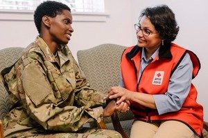 Red Cross volunteer speaking with young woman in military uniform