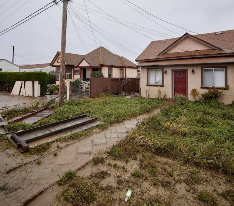 A home that has suffered minor damage, no standing water is visible but the ground is covered in mud..