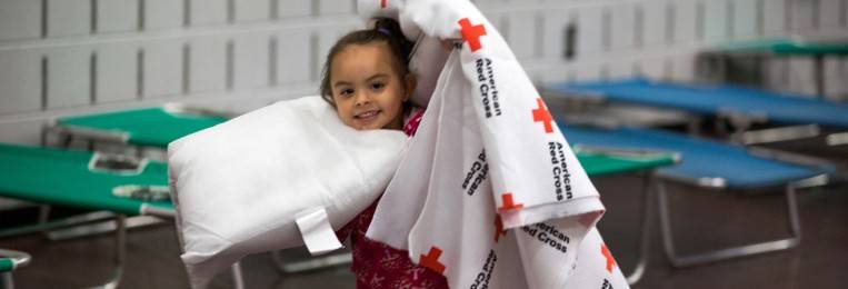 Little girl holding Red Cross blanket in a Red Cross shelter