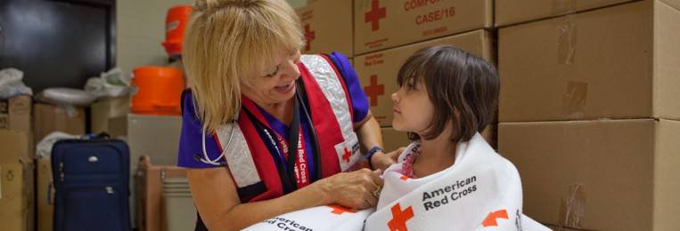 Red Cross volunteer comforting little girl in a shelter