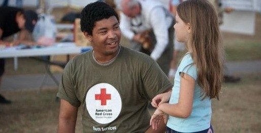 American Red Cross volunteer kneeling down and speaking to a child.