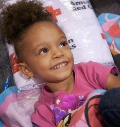 Fotografía de una niña sonriendo en una camilla de la Cruz Roja.