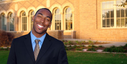 person in a suit smiling in front of a building