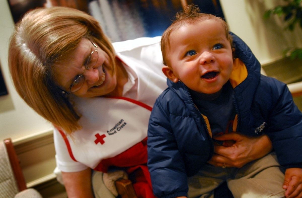 Red Cross volunteer holding a baby who is smiling.