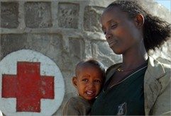 Person holding child with Red Cross logo painted on a brick wall.