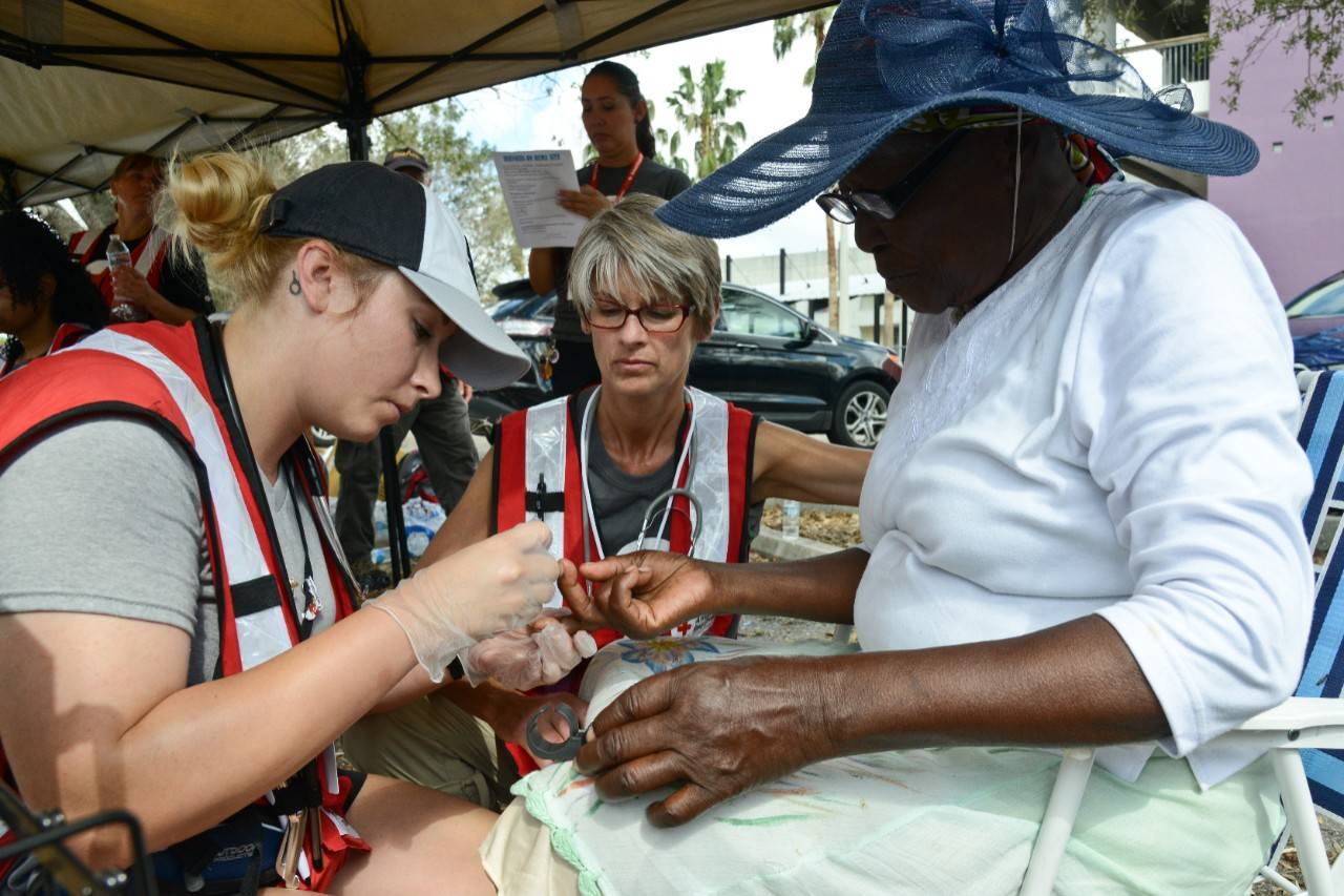 September 22, 2017. Immokalee, Florida. American Red Cross volunteer nurses, Summer (San Diego, California) and Toni (Burnsville, Minnesota), provide support to a resident of Immokalee, Florida.  Red Cross volunteer nurses were onsite providing health screenings – primary concerns were low blood sugar and dehydration.  Immokalee is the center of the region’s agriculture industry and home to many immigrant and migrant families, who primarily speak only Spanish and Creole.  Volunteer translators in both languages assisted residents receive care and much needed items. Photo by Daniel Cima for the American Red Cross