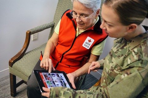 Red Cross volunteer looking at tablet with female military member