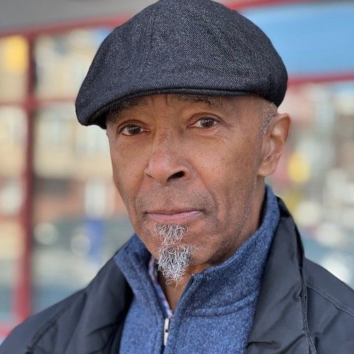 An older Black man wearing a cap looks to the camera.