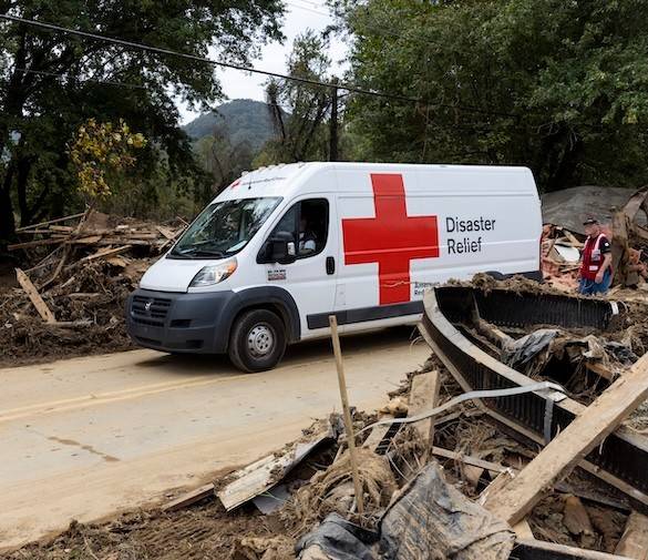 An emergency response vehicle is parked in front of damage from a hurricane.