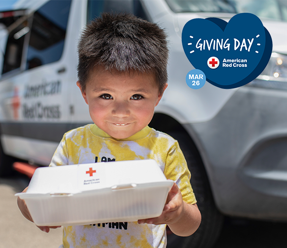A small child standing in front of an American Red Cross emergency response vehicle smiles while holding up a container of food. There is a logo in the top right corner reading Giving Day - American Red Cross, March 26
