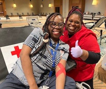 Smiling volunteer giving a thumbs up to the camera beside a donor