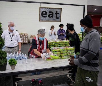 Volunteer in shelter hands out meals while standing underneath a sign that reads EAT
