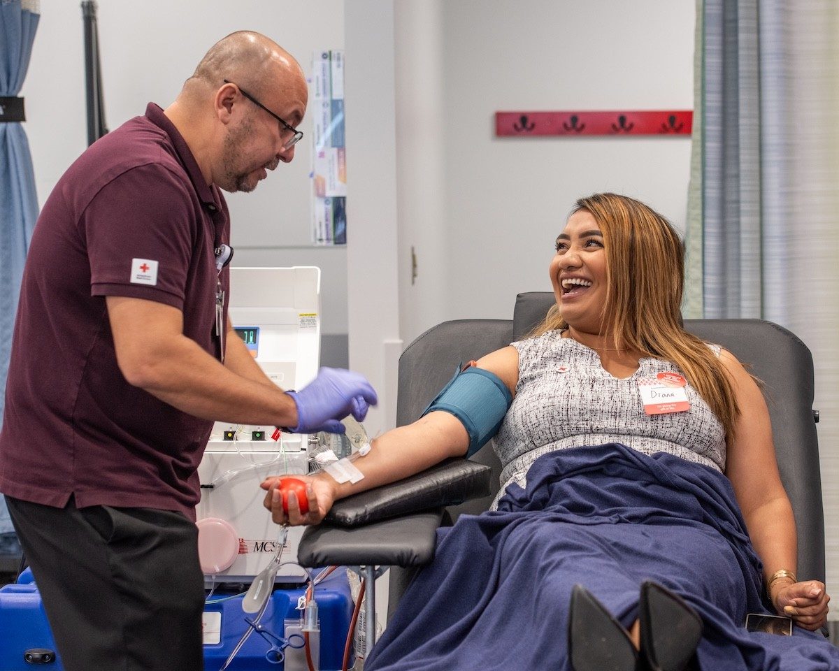 A donor reclines in a chair while a Red Cross staff member monitors a blood donation.