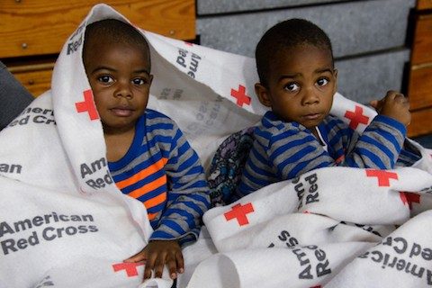 Two young boys under Red Cross blanket at shelter