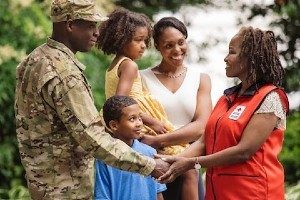 Red Cross volunteer speaking with young man in military uniform and his family