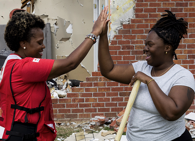 Two people giving a high five to each other in front of a demolished brick wall.