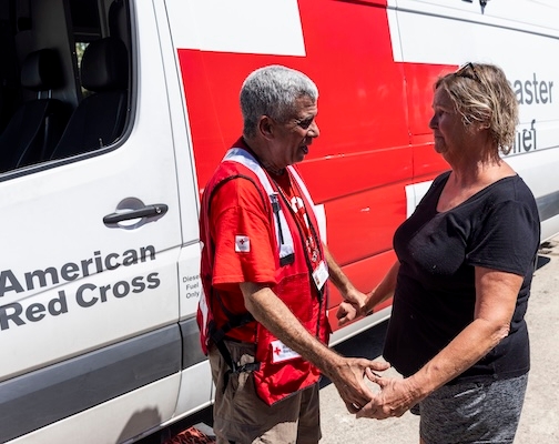 Red Cross volunteer holding hands with woman in front of Red Cross vehicle.